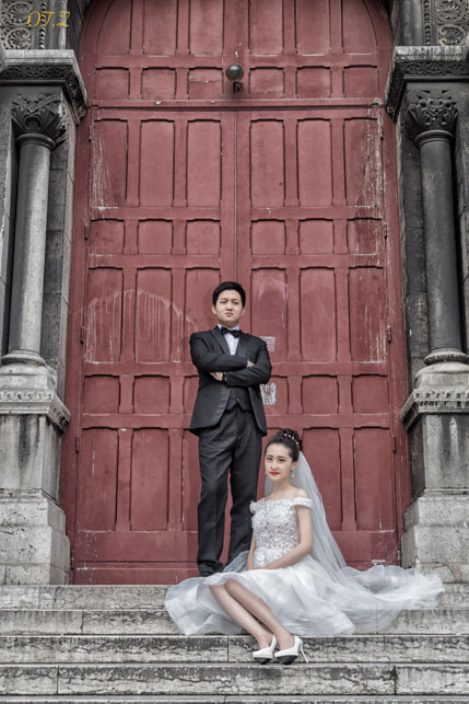 Couple de mariés posé sur des marches devant une porte d’église rouge