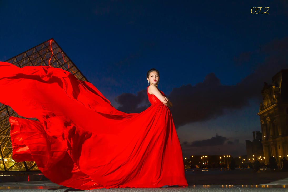 Femme en robe rouge fluide près de la pyramide du Louvre au crépuscule