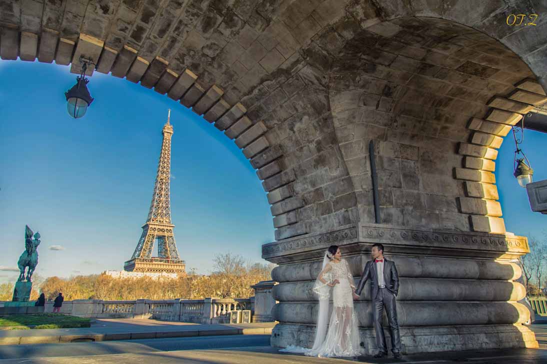 Couple de mariés sous une arche de pierre face à la tour Eiffel