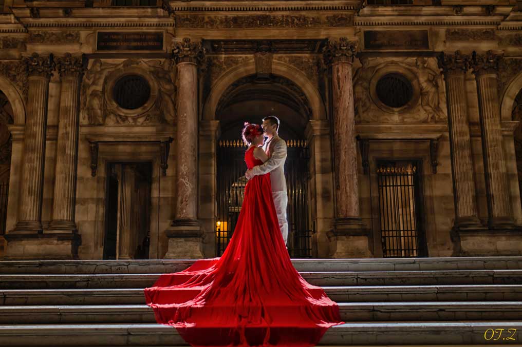 Femme en robe rouge sur les marches d’un monument parisien de nuit